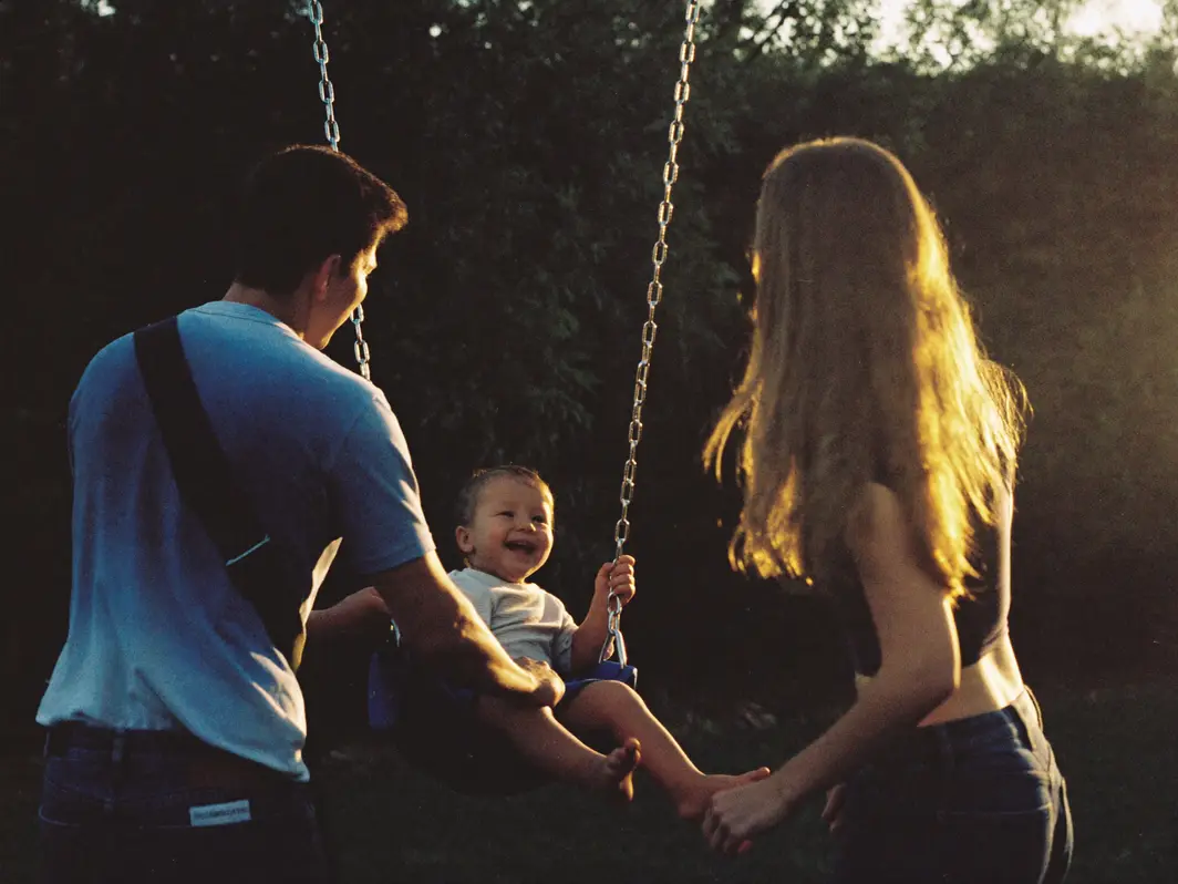 Parents pushing their laughing child on a backyard swing at golden hour